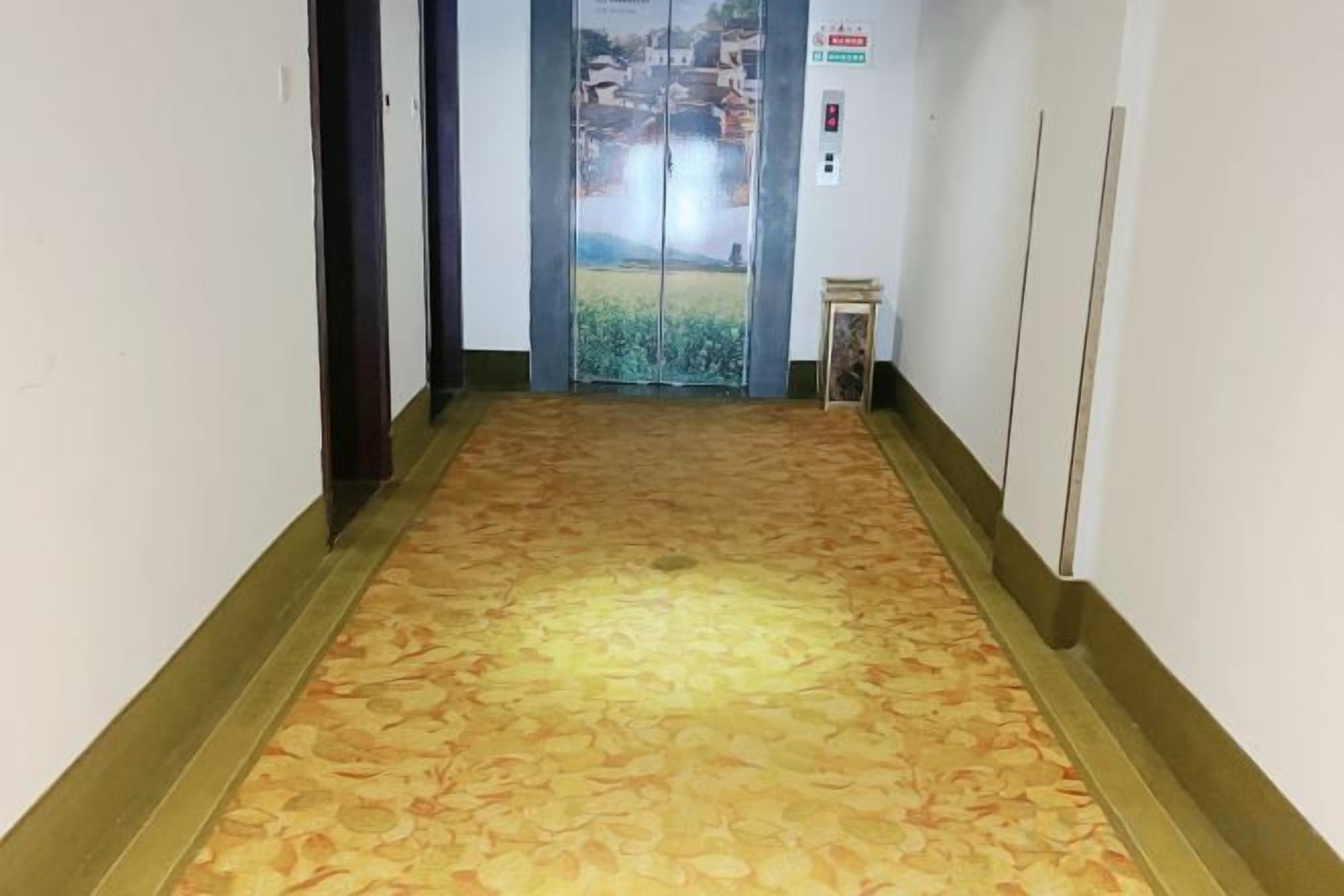 A hallway with patterned carpet, a glass elevator door, and a small table with a sign.