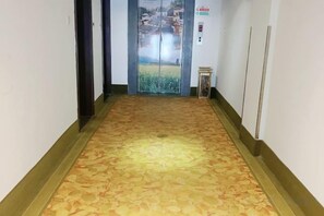 A hallway with patterned carpet, a glass elevator door, and a small table with a sign.