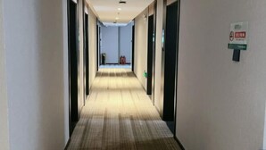 A hotel corridor with a carpeted floor, doors on both sides, and a fire extinguisher visible in the distance. - GreenTree Inn Jiangxi Shangrao Wuyuan Bus Station Tang Village Express Hotel (Wuyuan)