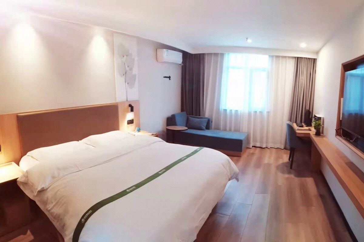 Habitación de hotel con cama, escritorio, silla, televisor y ventana con cortinas.