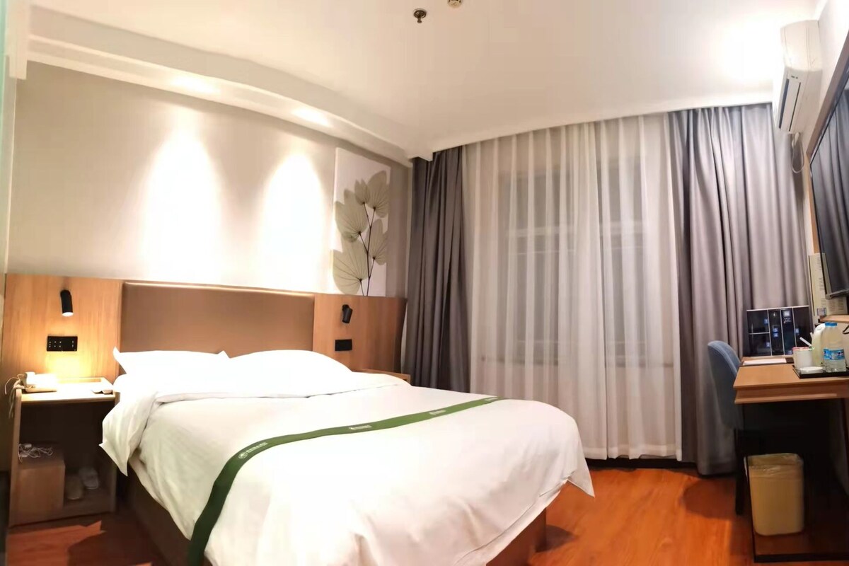 Una habitación de hotel con cama, escritorio, silla, televisor y ventana con cortinas.