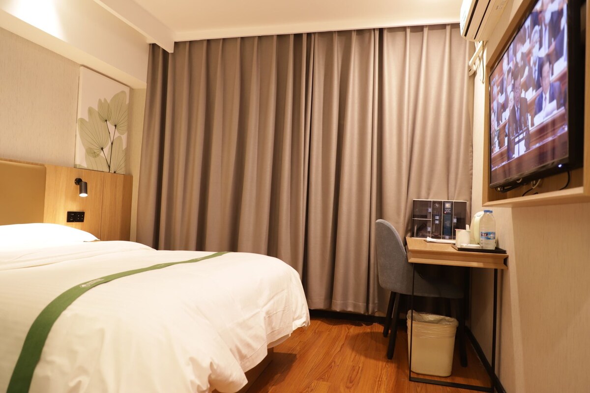 Una habitación de hotel con una cama, un escritorio, una silla, un televisor y un cesto de basura.
