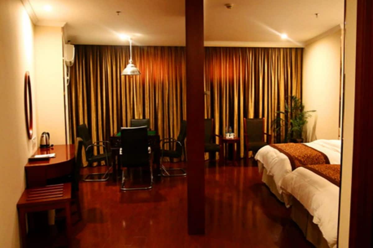 Ein Hotelzimmer mit einem Bett, einem Schreibtisch mit Stuhl, einem kleinen Tisch und einer Zimmerpflanze.