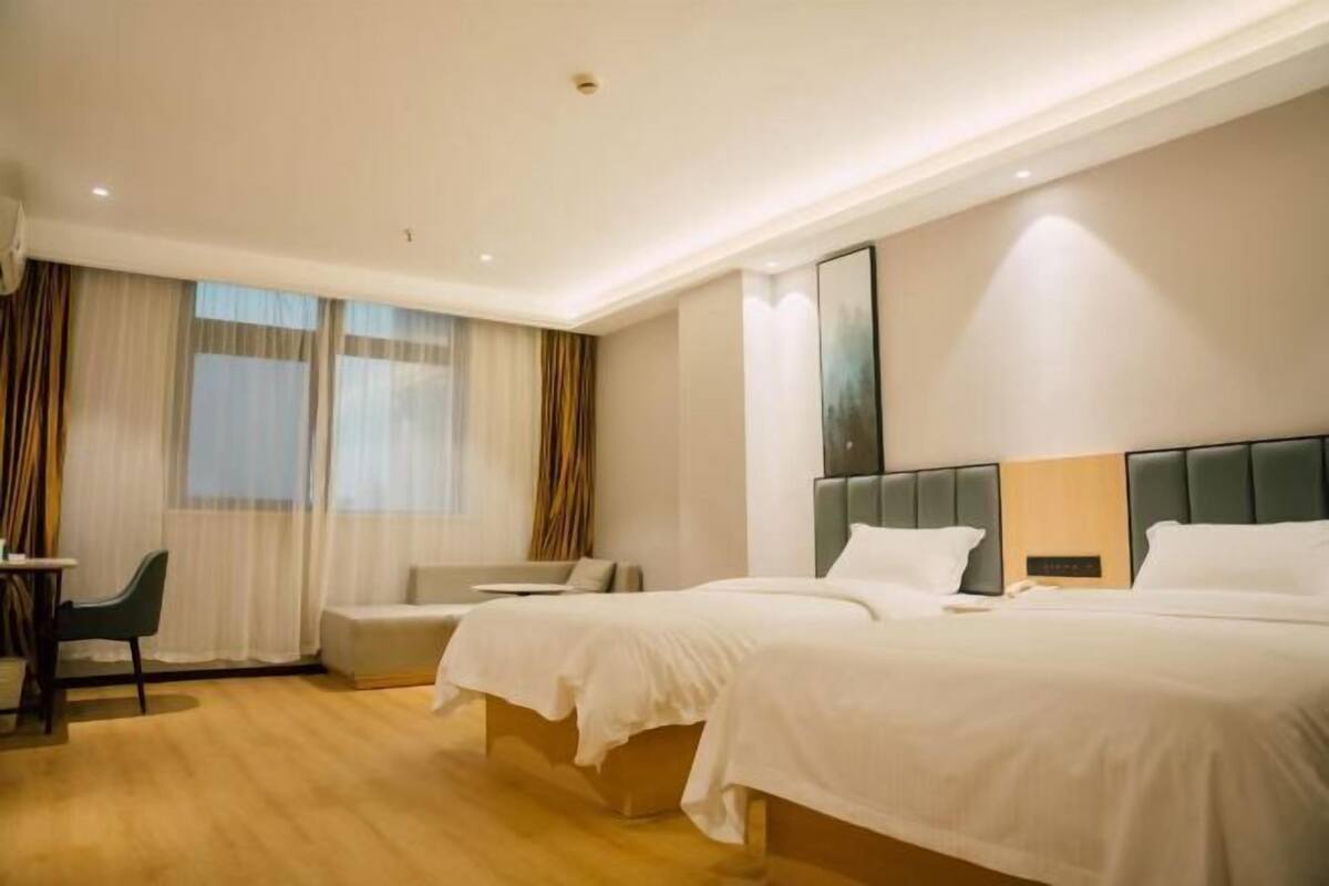 Ein Hotelzimmer mit zwei Betten, einem Schlafsofa, einem Schreibtisch und einem Fenster mit Vorhängen.