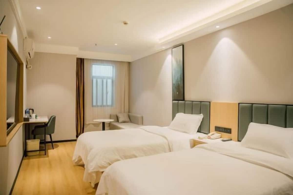 Ein Hotelzimmer mit zwei Betten, einem Schreibtisch, einem Stuhl, einem kleinen Tisch und einem Fenster mit Vorhängen.
