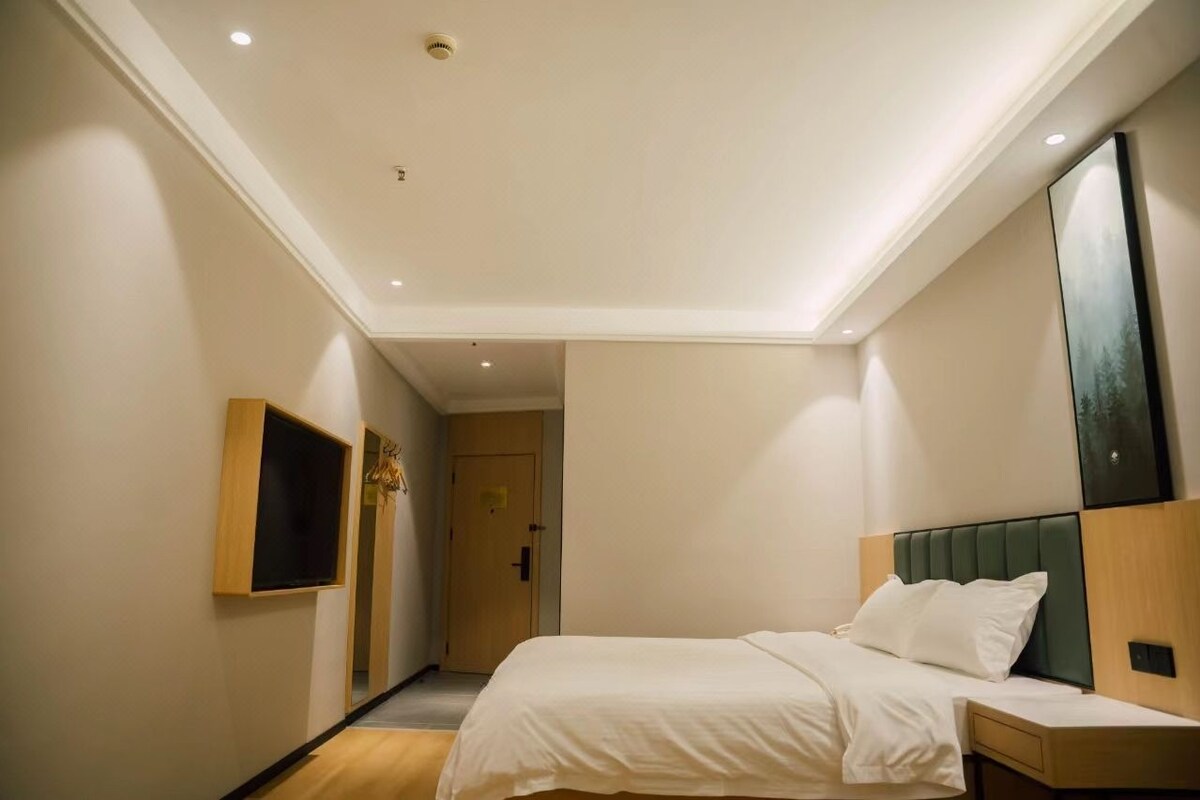 Habitación de hotel con cama, mesita de noche, televisor montado en la pared y puerta que da a otra habitación.