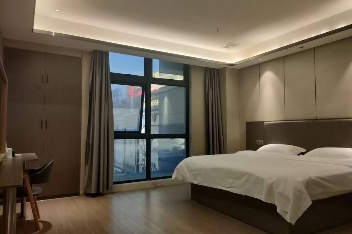 Ein modernes Hotelzimmer mit einem großen Bett, einem Schreibtisch und Blick durch ein großes Fenster.