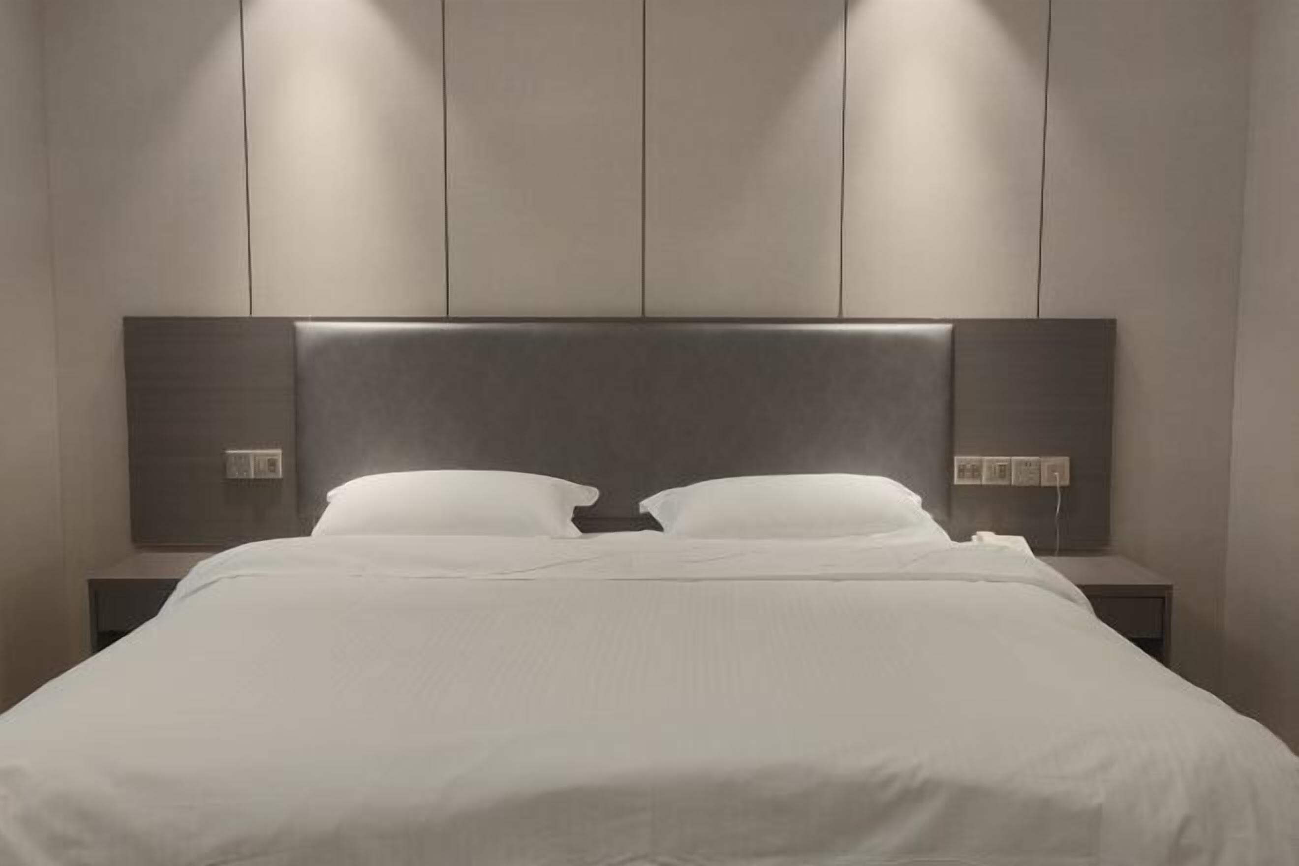 Una habitación de hotel moderna con una cama grande, dos mesitas de noche y una paleta de colores neutros.
