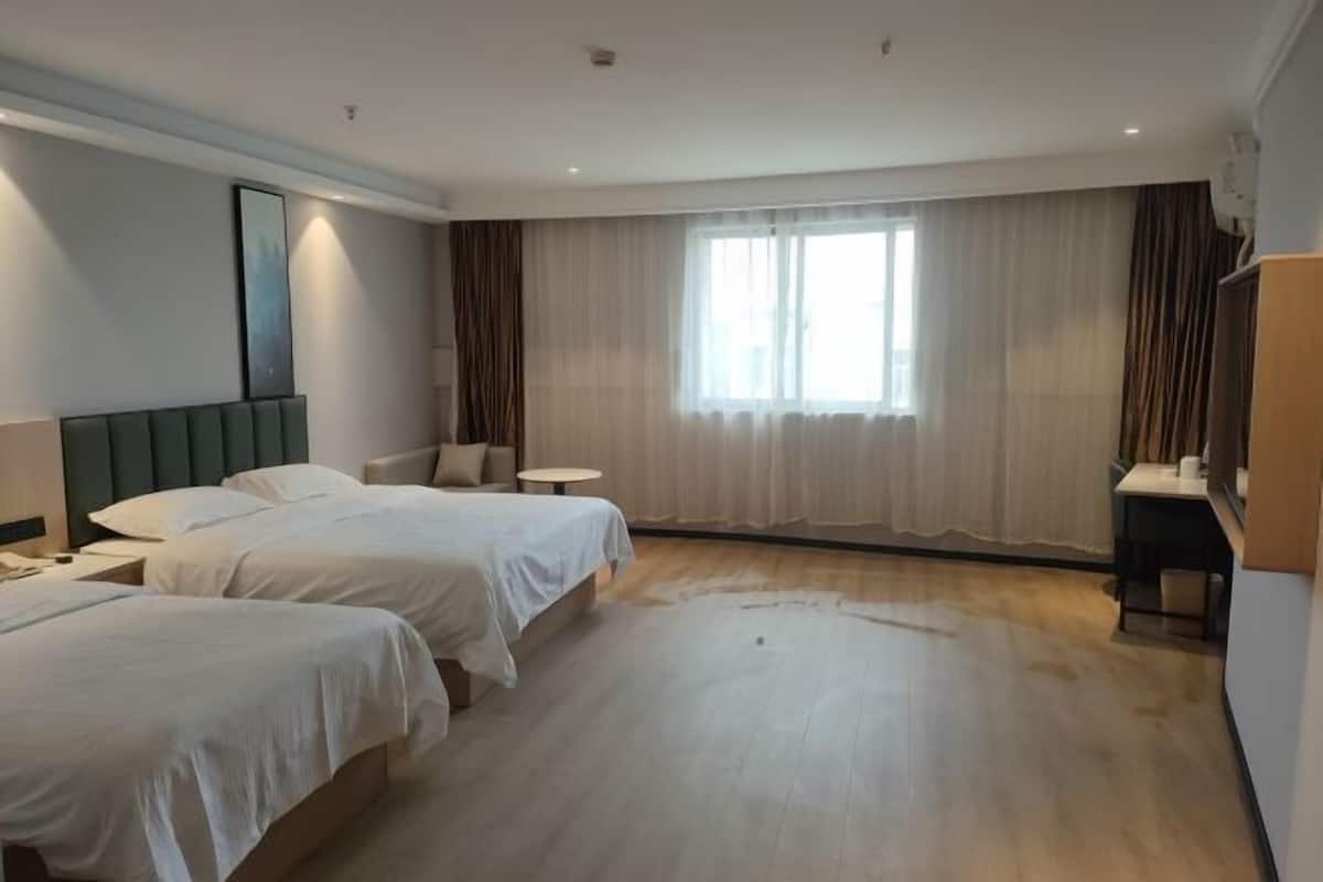 Ein Hotelzimmer mit zwei Betten, einem kleinen runden Tisch, einem Schreibtisch und einem großen Fenster mit Vorhängen.
