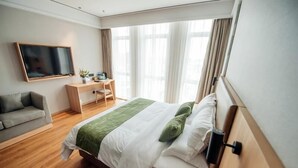 Une chambre d’hôtel équipée d’un lit, d’un bureau, d’une chaise, d’un canapé, d’une télévision et d’une fenêtre avec des rideaux.
