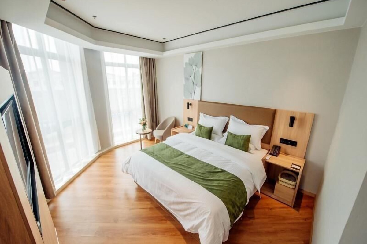Una habitación de hotel moderna con una cama grande, una mesita de noche, una silla y una ventana con cortinas.