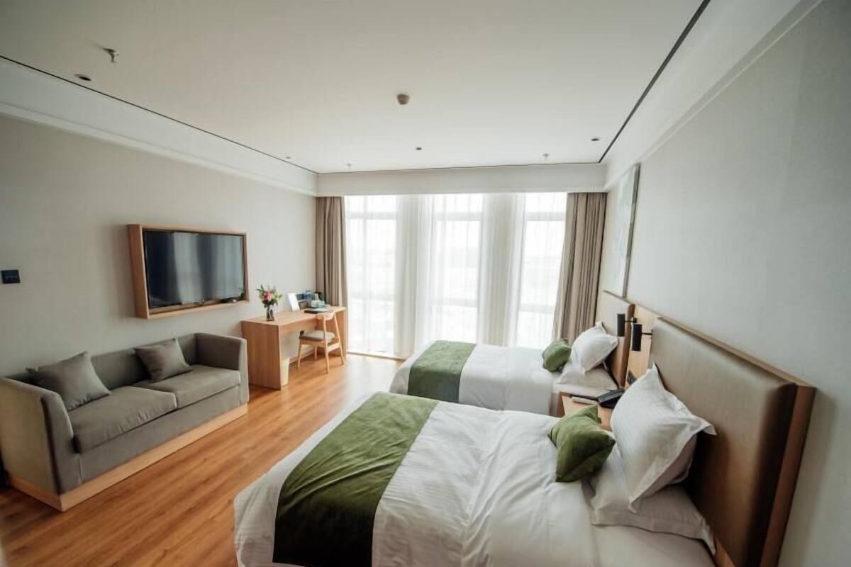 A hotel room with two beds, a desk, a sofa, and a TV.