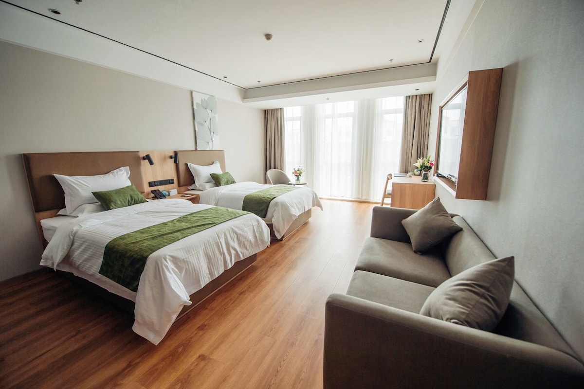 Habitación de hotel con dos camas, un sofá, un escritorio y un ventanal con cortinas.