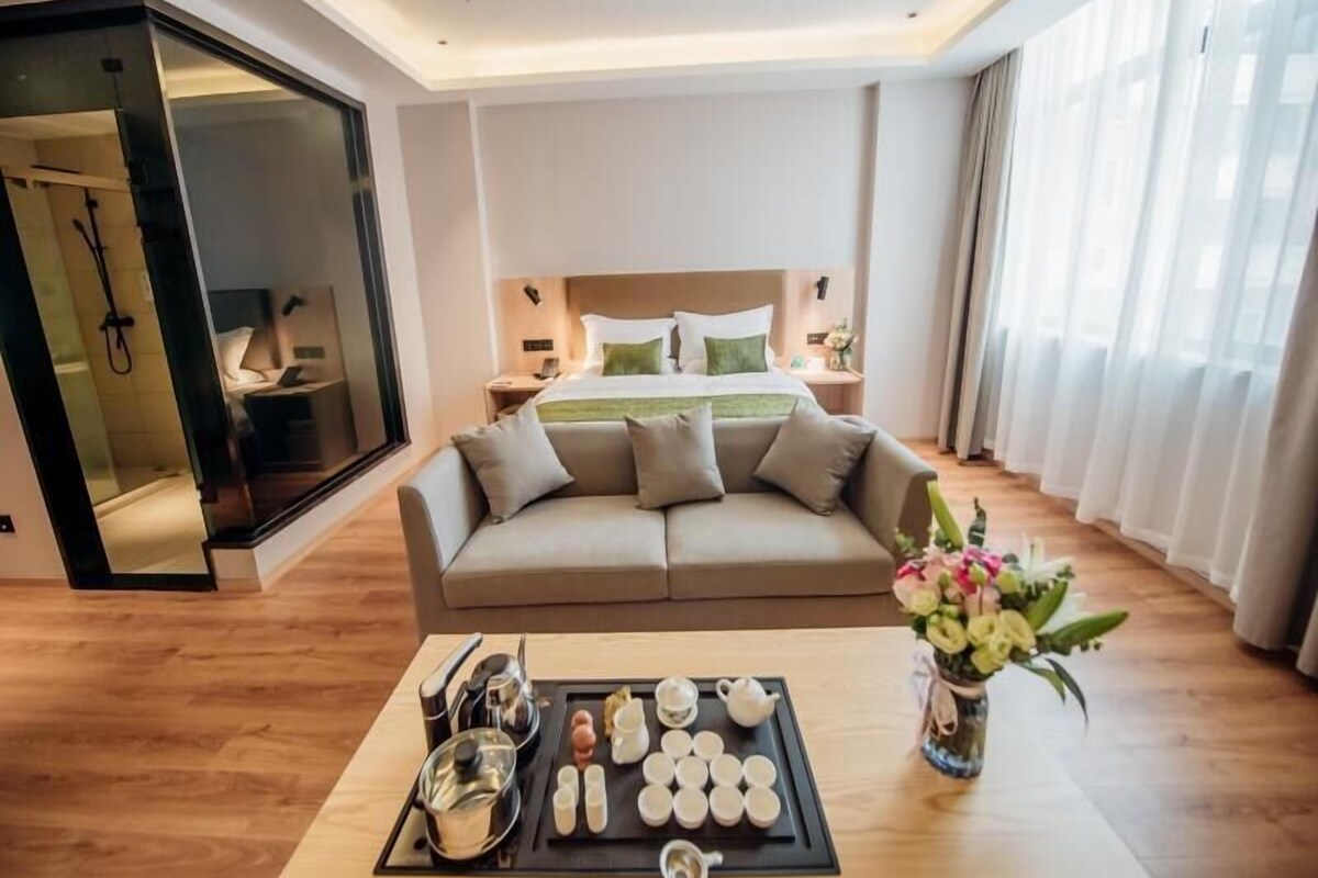 A hotel room with a bed, a sofa, a table with tea set, and a vase with flowers.
