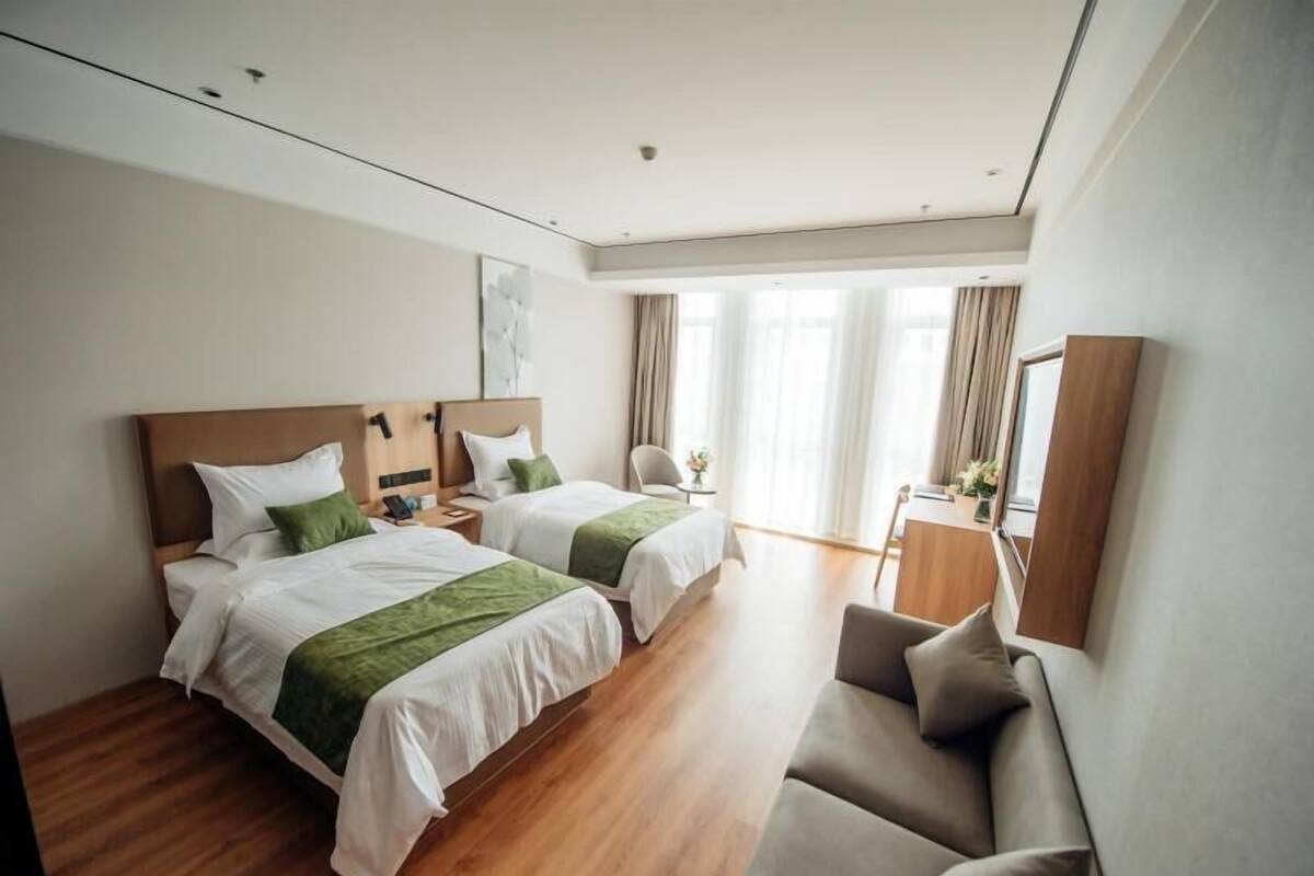 A hotel room with two beds, a sofa, a desk, and a large window.