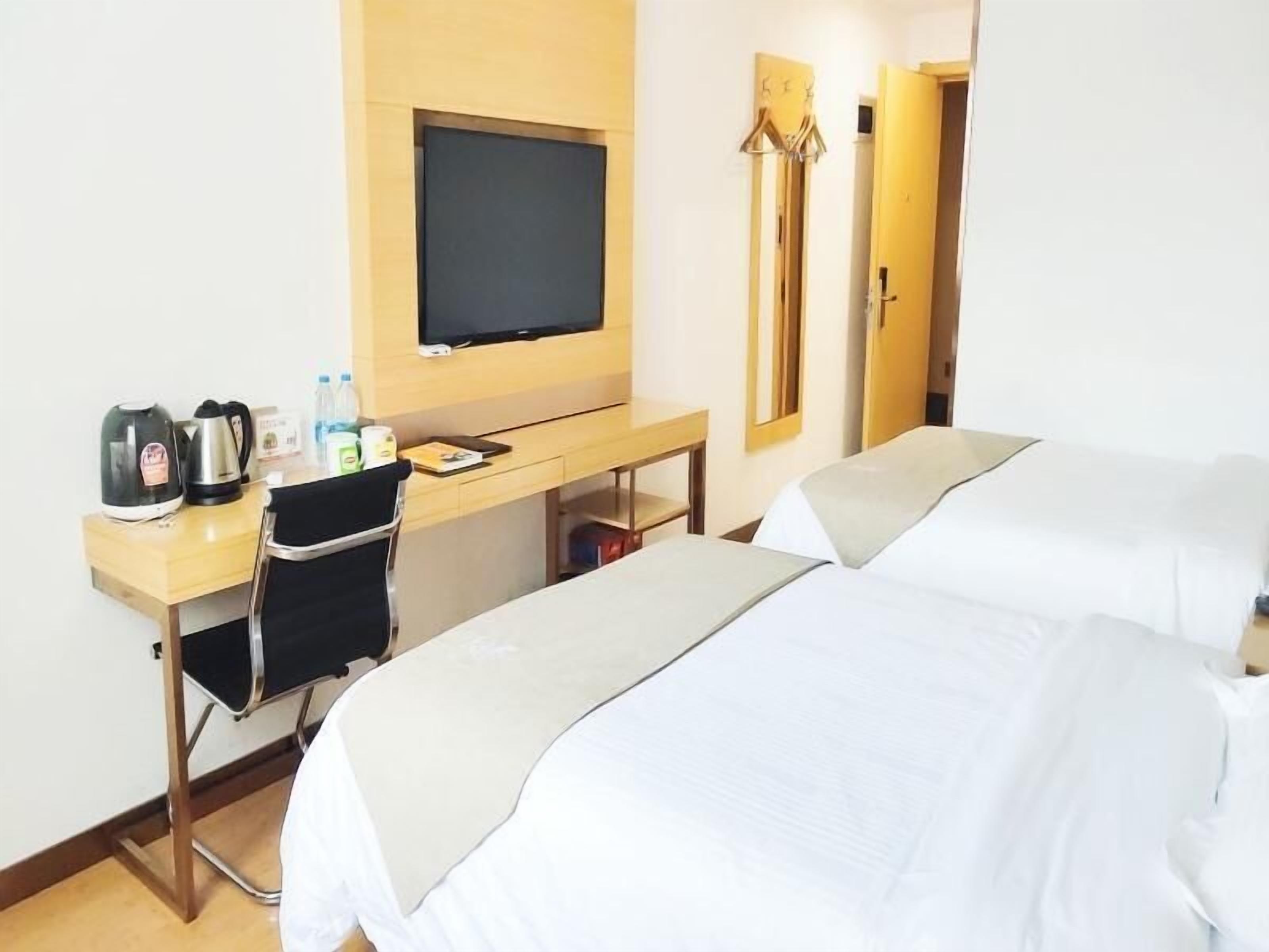 A hotel room with two beds, a desk with a television, a chair, and a coat rack.