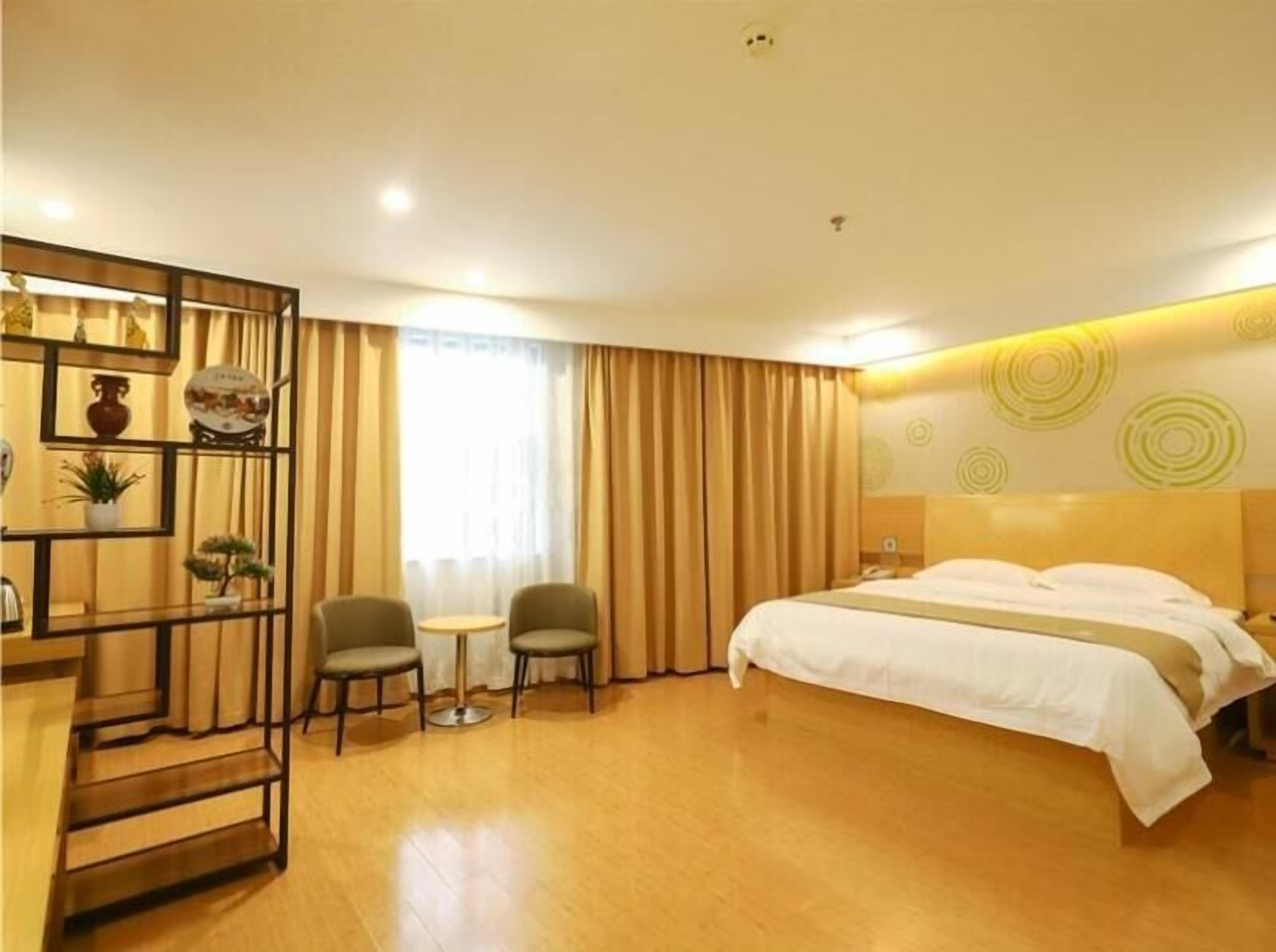 A hotel room with a bed, two chairs, a small table, and a decorative shelf.