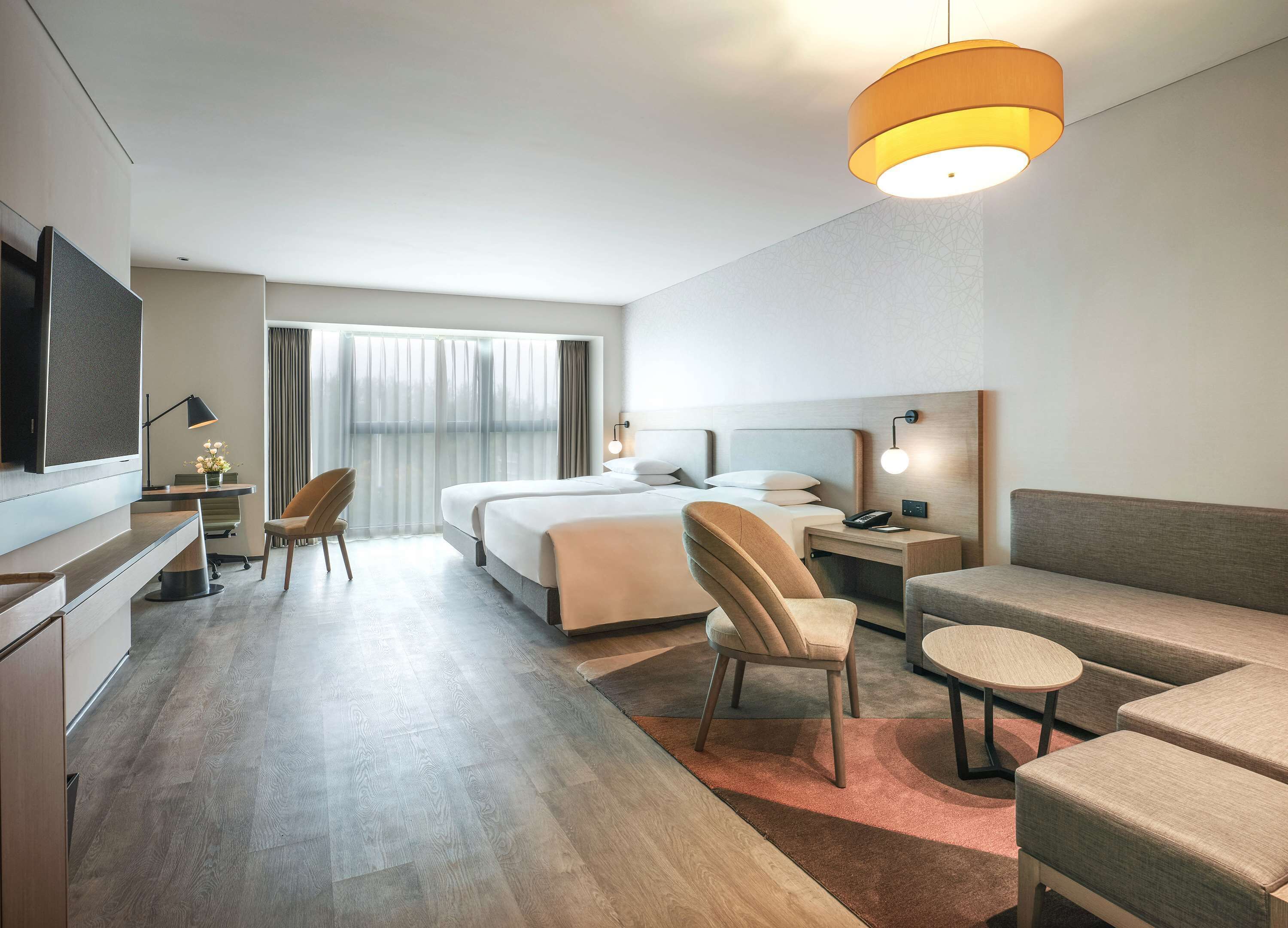 A modern hotel room with a large bed, a desk, a chair, a sofa, and a TV.