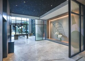 A modern lobby with a starry ceiling, a large leaf artwork, and a seating area with a bench and chairs.