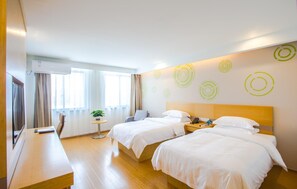 A hotel room with two beds, a small table with a plant, a desk, and a wall with circular patterns. - Greentree Inn Jiaxing Qixing Town Goverment (Jiaxing)