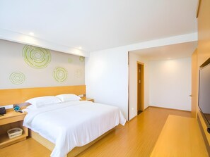 A modern hotel room with a wooden bed, a bedside table with a phone and a lamp, and a wall with circular patterns. - Greentree Inn Jiaxing Qixing Town Goverment (Jiaxing)
