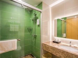 Un bany amb rajoles verdes, una cabina de dutxa de vidre, un lavabo amb taulell de marbre i una porta de fusta.