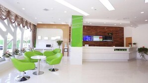 Un espace d’accueil moderne avec un comptoir de réception en bois, des chaises vertes et une grande fenêtre agrémentée de rideaux.