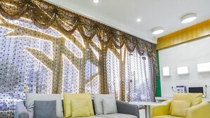 Un espace d’accueil avec un canapé gris et un fauteuil jaune, un rideau décoratif et un comptoir d’accueil.
