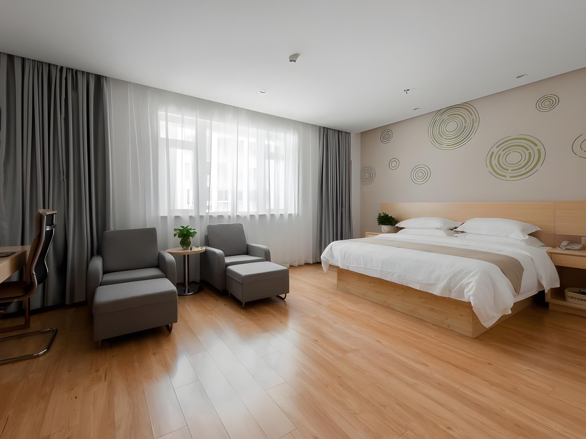 Una habitación de hotel moderna con una cama grande, dos sillones, una mesita con una planta y un escritorio con una silla.