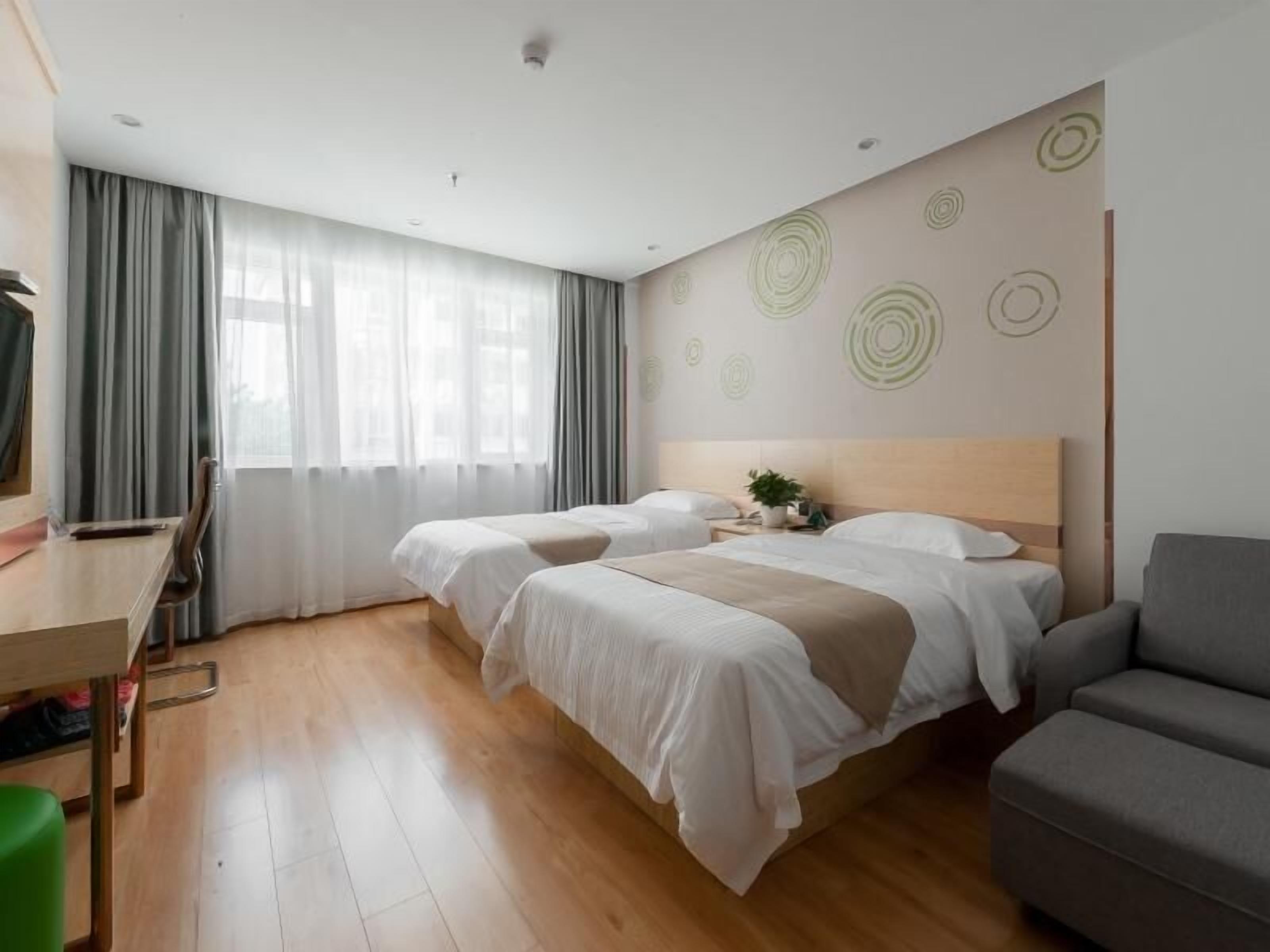 A hotel room with two beds, a desk, a chair, and a sofa.