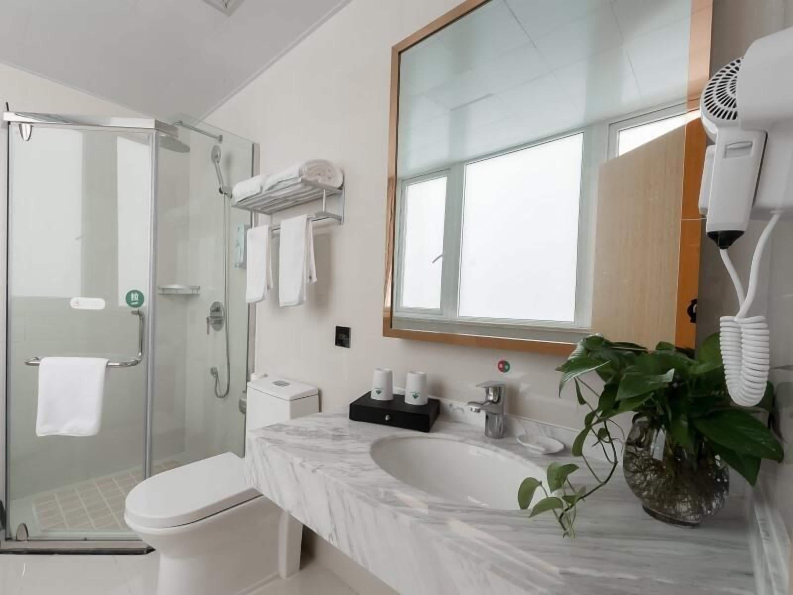 Ein modernes Badezimmer mit Duschkabine aus Glas, Toilette in Weiß, Marmorwaschbecken und einem großen Spiegel.