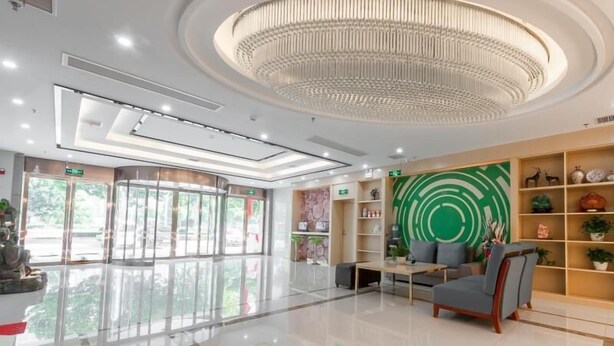 Un hall d’entrée spacieux agrémenté d’un lustre moderne, un coin salon avec un canapé et des fauteuils, et un mur décoratif orné d’un motif circulaire vert.
