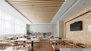 Un espace repas moderne avec des tables et des chaises en bois, une cuisine en arrière-plan et un téléviseur à écran plat fixé au mur.