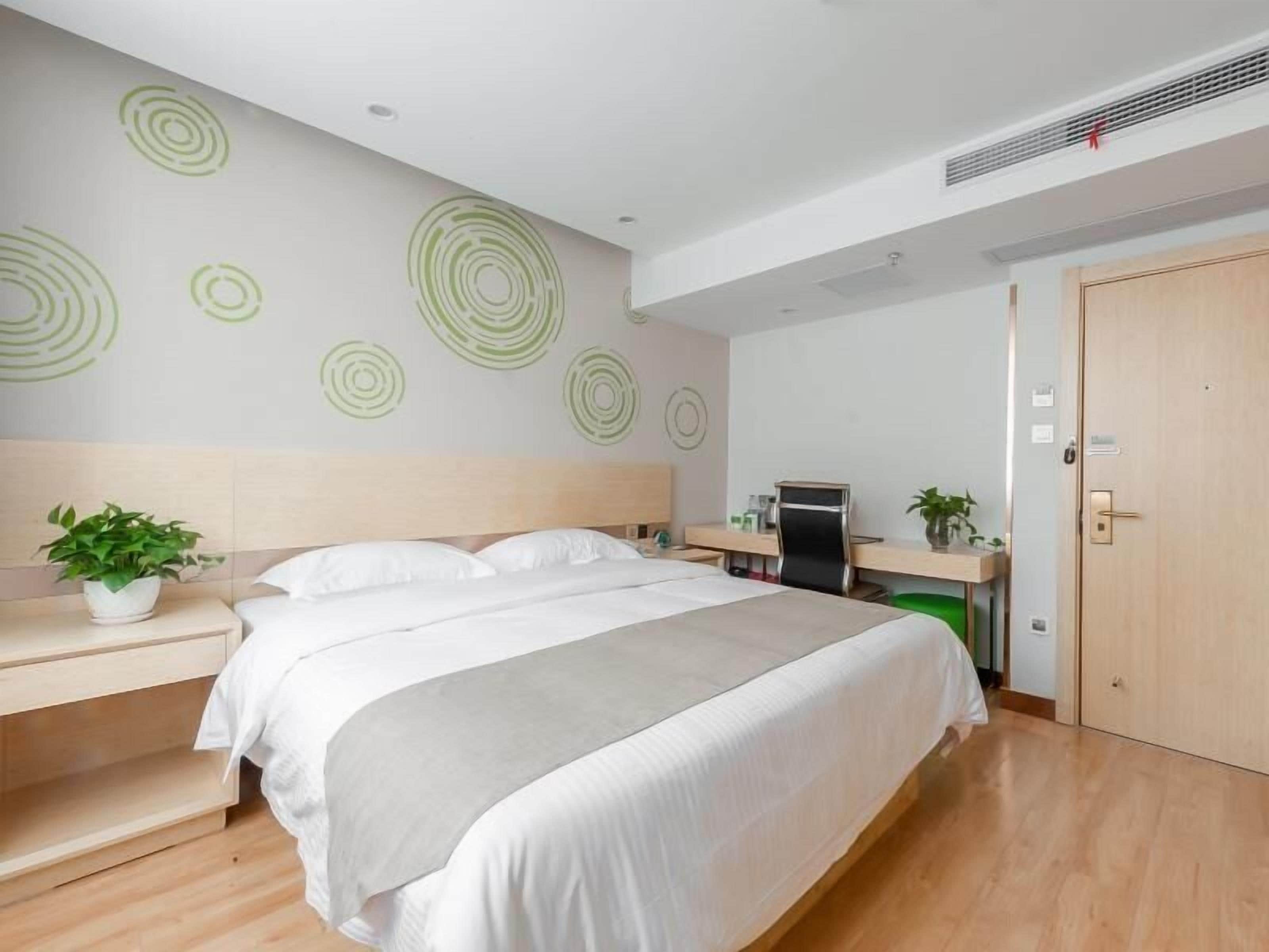 Ein modernes Hotelzimmer mit einem großen Bett, einem Schreibtisch, einem Sessel und einer kleinen Pflanze.