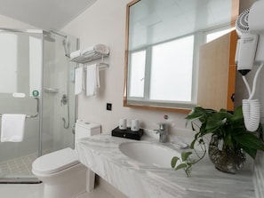 Een moderne badkamer met een glazen douche, wit toilet, marmeren wastafel en een grote spiegel.