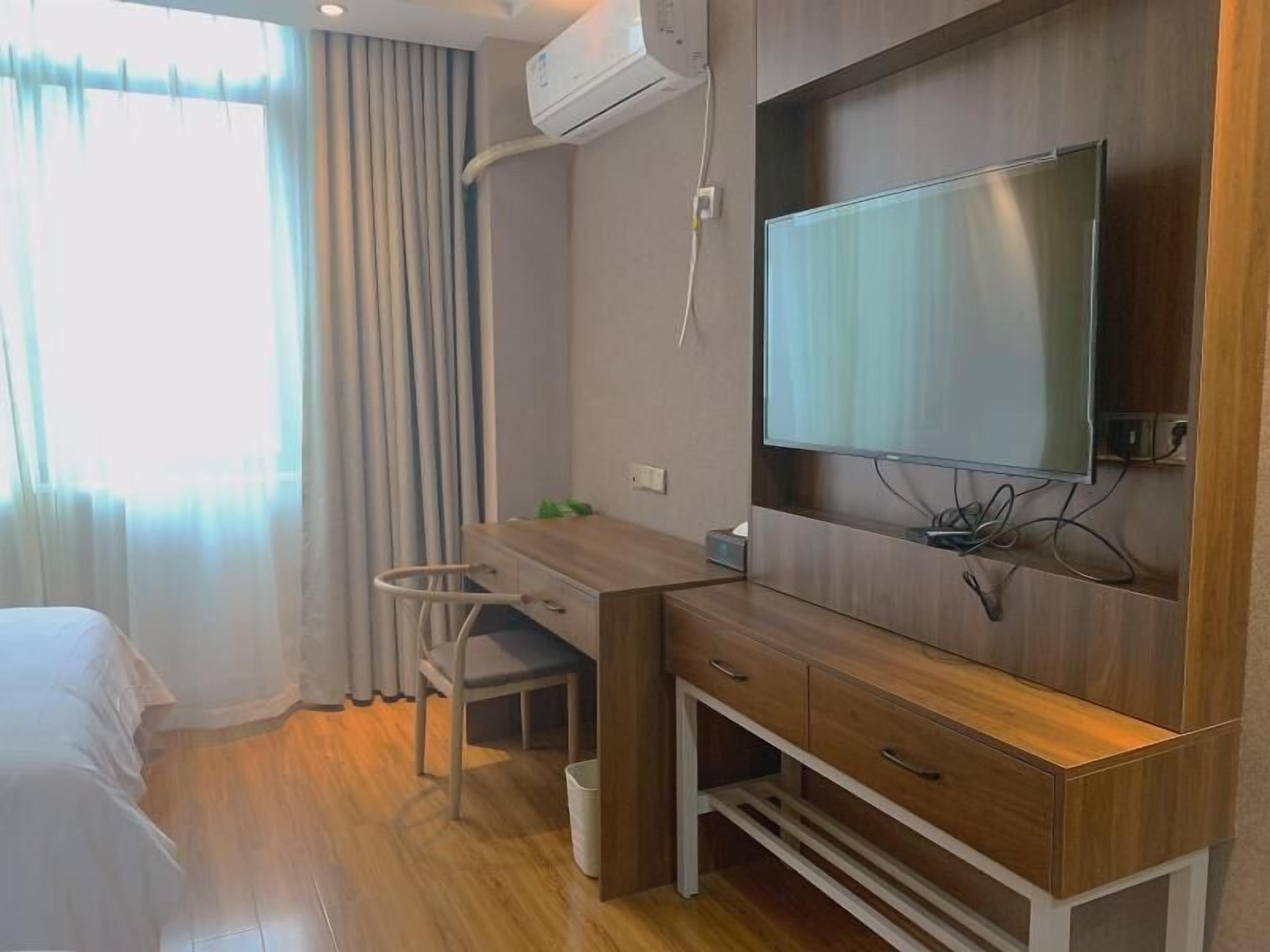A hotel room with a wooden desk, a chair, a TV mounted on the wall, and a bed.