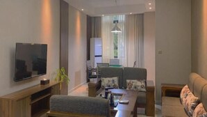 A modern living room with a flat-screen TV, a sofa, a coffee table, and a chandelier. - Greentree Inn Shangrao Yueliangwan Automobile City (Shangrao)