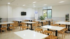 A spacious dining area with multiple tables and chairs, a flat-screen TV mounted on the wall, and a window providing natural light. - Greentree Inn Shangrao Yueliangwan Automobile City (Shangrao)