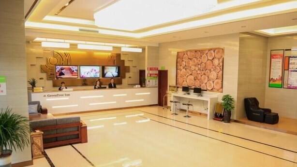 A hotel reception area with a modern design, including a reception desk, seating area, and a wall with a wood-like pattern. - Greentree Inn Shangrao Yueliangwan Automobile City (Shangrao)