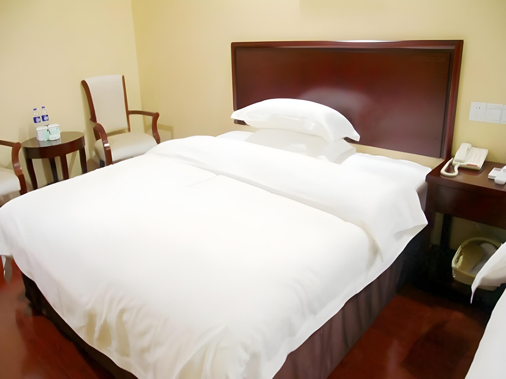A hotel room with a large bed, a wooden headboard, a bedside table with a phone, and a chair.
