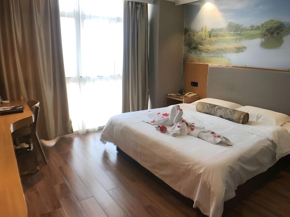 Una habitación de hotel con una cama grande, un escritorio y un cuadro de un paisaje en la pared.