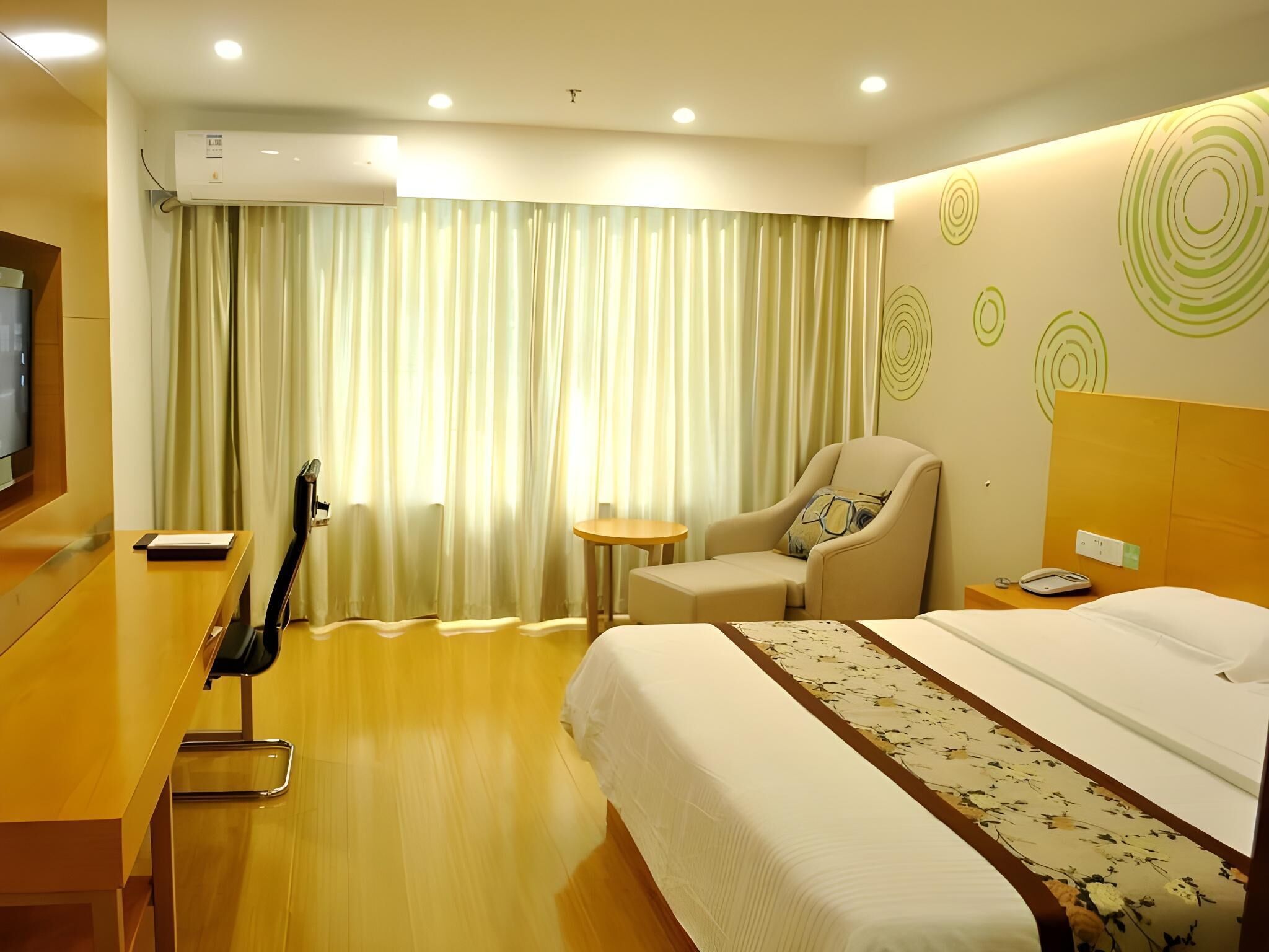 A hotel room with a bed, a chair, a desk, a television, and a window with curtains.