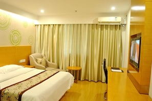Una habitación de hotel con una cama, una silla, una mesita pequeña, un aire acondicionado y un televisor.