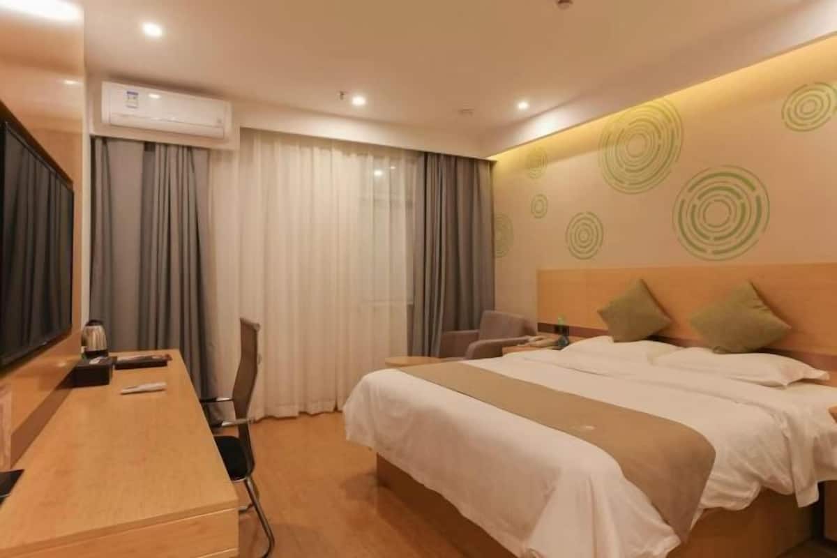 A hotel room with a bed, a desk, a chair, an air conditioning unit, and a curtain.