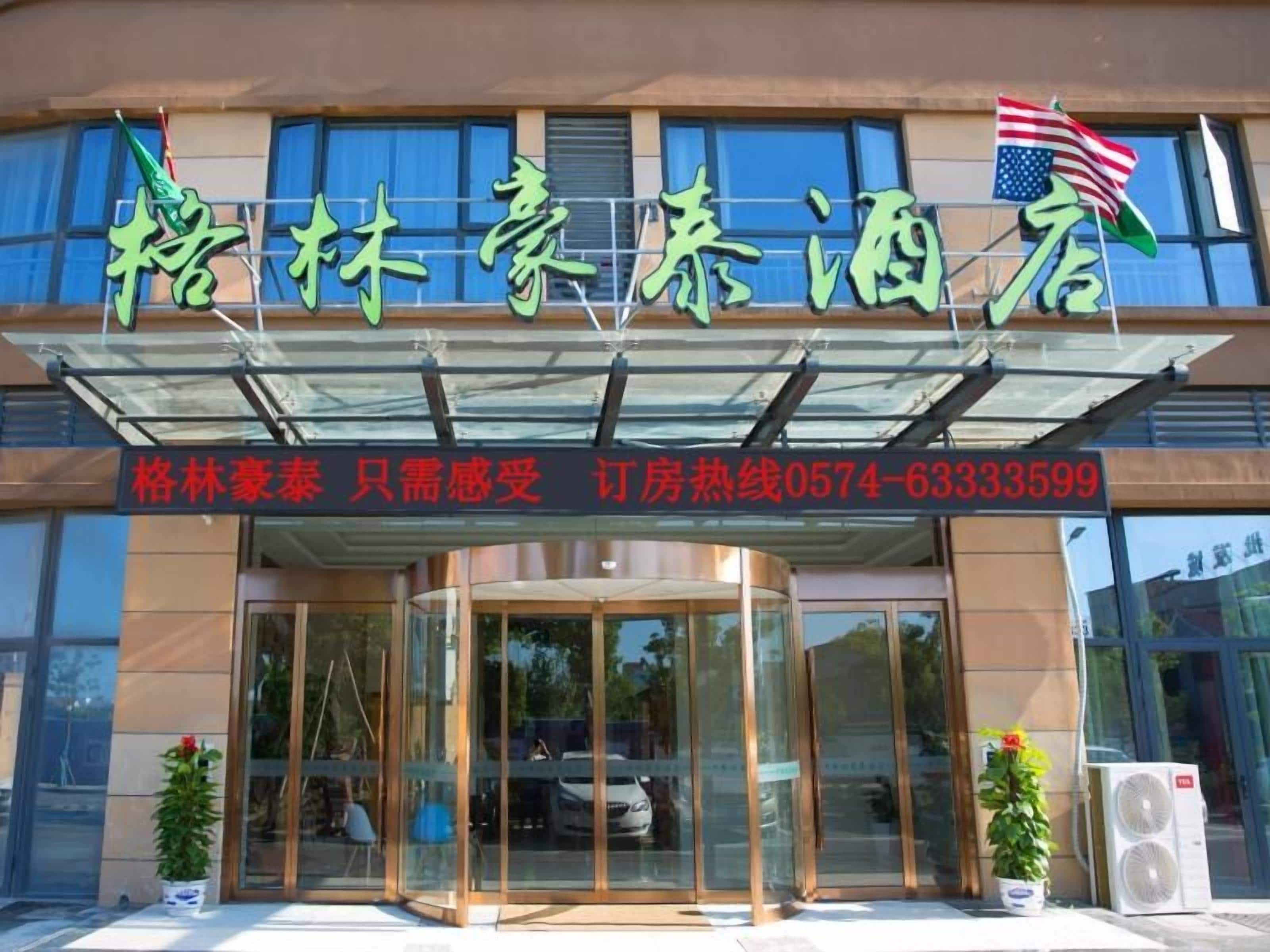 A hotel entrance with a glass facade, a signboard with Chinese characters, and an American flag.