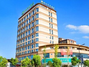 Un hotel de varios pisos con fachada curva, numerosas ventanas y un letrero verde que indica un restaurante o comedor.