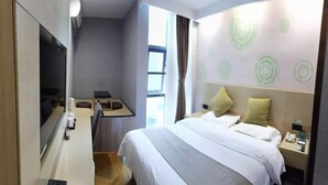 Quarto de hotel com cama, escrivaninha, cadeira, televisão e janela.