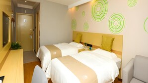 Quarto de hotel com duas camas, uma escrivaninha e uma cadeira. Há decalques circulares verdes na parede.