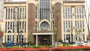 Um edifício de vários andares com entrada central, grandes janelas e aparelhos de ar condicionado.