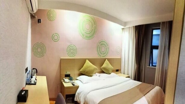 Quarto de hotel com cama, escrivaninha, cadeira, mesa de cabeceira e parede com padrões circulares.
